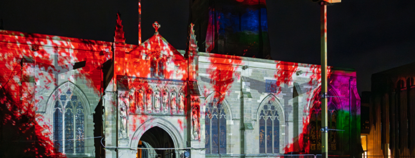 St. Mary de Castro Church illuminated with vibrant red and multicolor projections during Light Up Leicester 2025, creating a mesmerizing fusion of history and modern digital art.