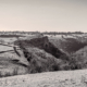 A monochrome landscape of the Peak District, featuring the dramatic limestone cliffs near Thor’s Cave, surrounded by rolling hills and dry stone walls.
