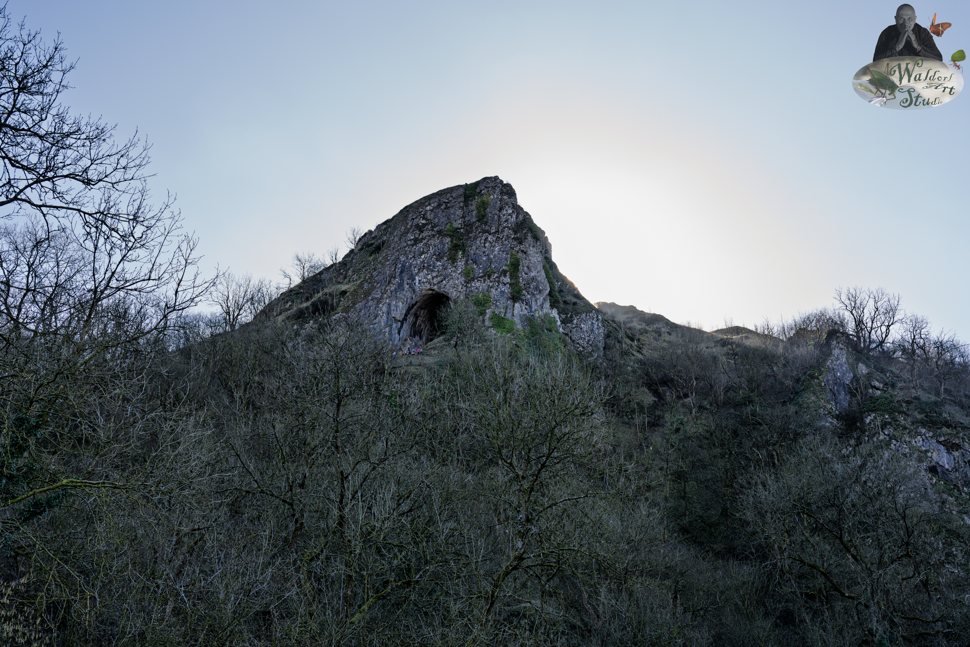 A breathtaking view of Thor’s Cave, a towering limestone hill with its iconic cavern entrance, nestled among leafless trees in the heart of the Peak District National Park.