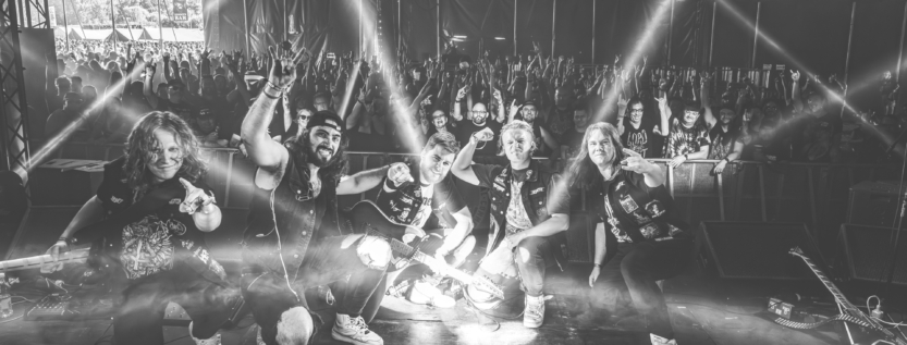 Rascal posing with the crowd at Bloodstock 2025 in a dramatic black-and-white shot, beams of light crossing the stage.