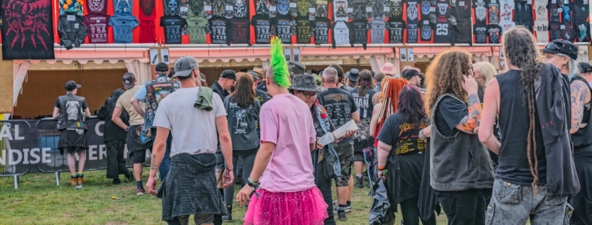 Festivalgoers browsing official band merchandise at Bloodstock Open Air 2025, crowd gathered in front of metal festival merch stalls