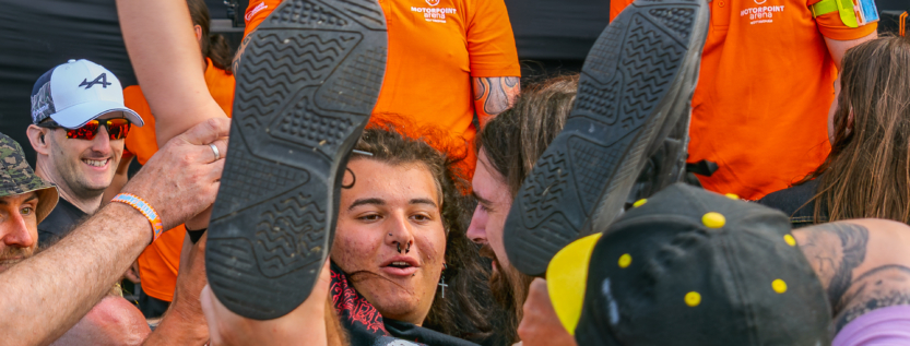 Crowd surfer being supported by fans and watched by event security in orange shirts during Shrapnel’s set at Bloodstock Open Air Festival