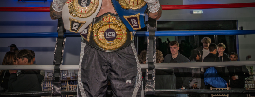 Boxing champion standing in the ring holding multiple ICB title belts after a victorious fight at the Derby Boxing Gala. Captured by Waldorf Art Studio, UK sports photographer.