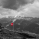 Black and white alpine landscape with a Swiss flag in red standing above a valley and distant mountain range under dramatic clouds